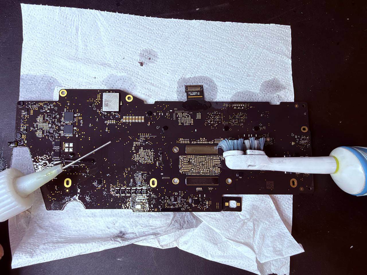 Limpieza manual controlada de la placa lógica de un MacBook Pro M2 afectado por líquido