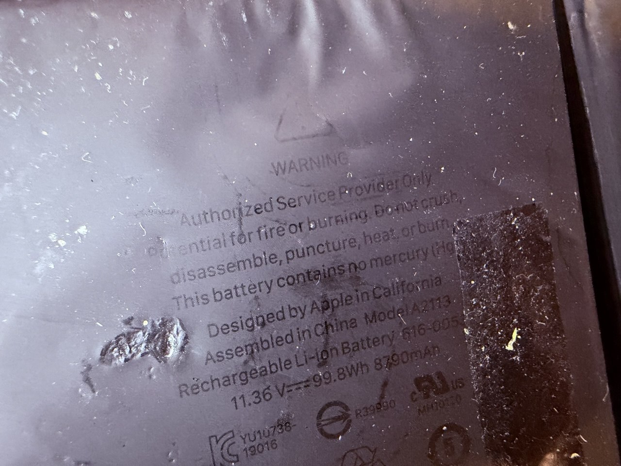 Batería Apple A2113 de MacBook Pro 16 hinchada — etiqueta de advertencia visible con deformación