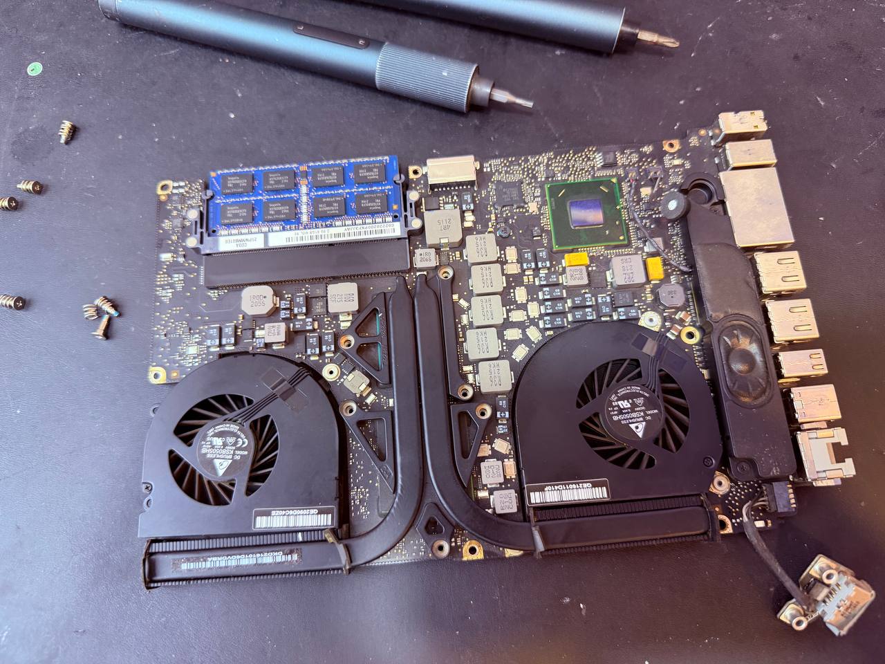 Placa base MacBook Pro extraída sobre mesa de trabajo con ventiladores y RAM