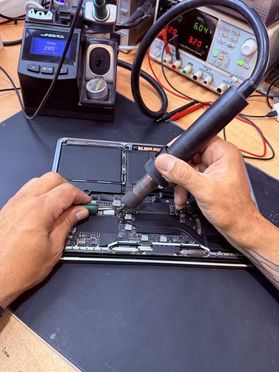 Técnico de ReciclaTecnología aplicando aire caliente con la estación de microsoldadura sobre la placa base de un MacBook abierto, en el taller de Sant Antoni, Barcelona