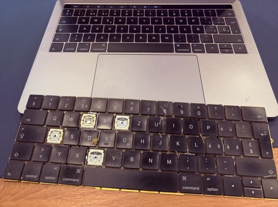 MacBook Pro encendido con el teclado nuevo montado y el teclado antiguo apoyado delante